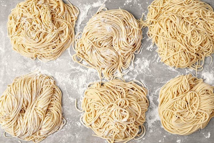 Six nests of raw spaghetti pasta arranged on a floured surface.
