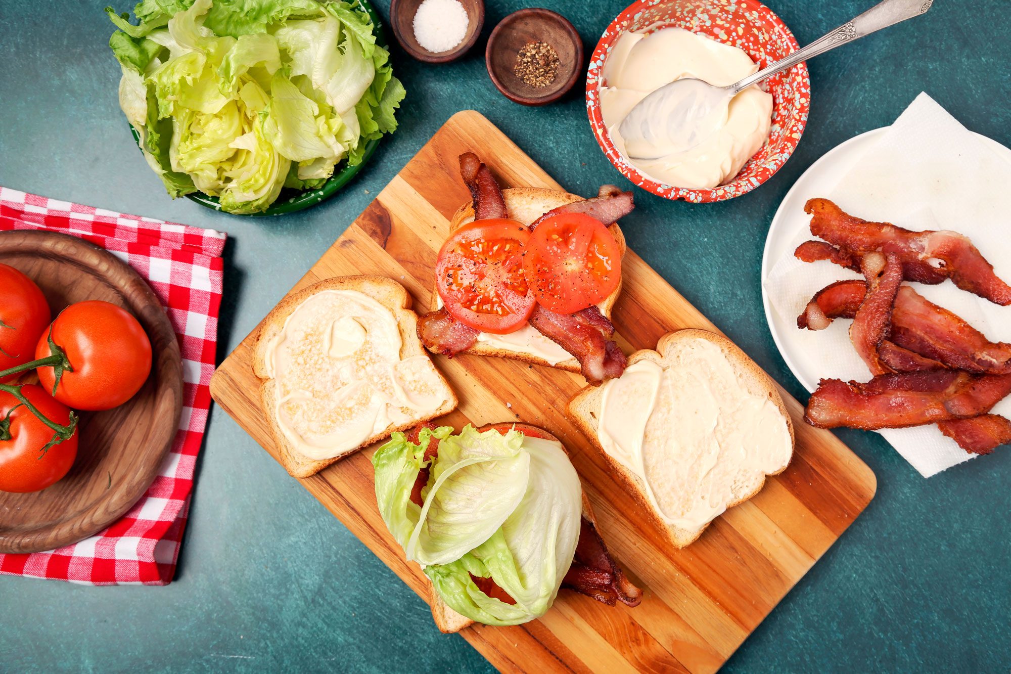 How to push pull image of Taste of Home's BLT shot on a blue green surface. Assembling the sandwich with toasted bread mayo and bacon.