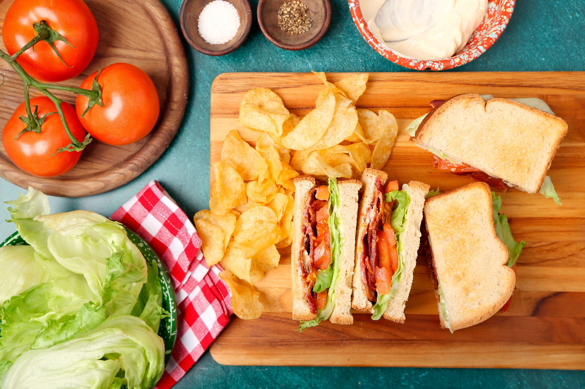 Cover pull push image of Taste of Home's BLT shot on a blue green surface. Assembled BLT sliced and served on a wooden surface.