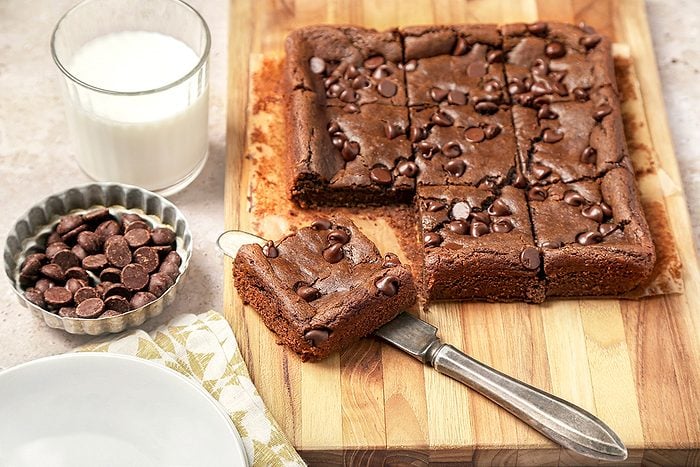 A batch of Chickpea chocolate brownies on a wooden board, cut into squares. One piece is on a knife.