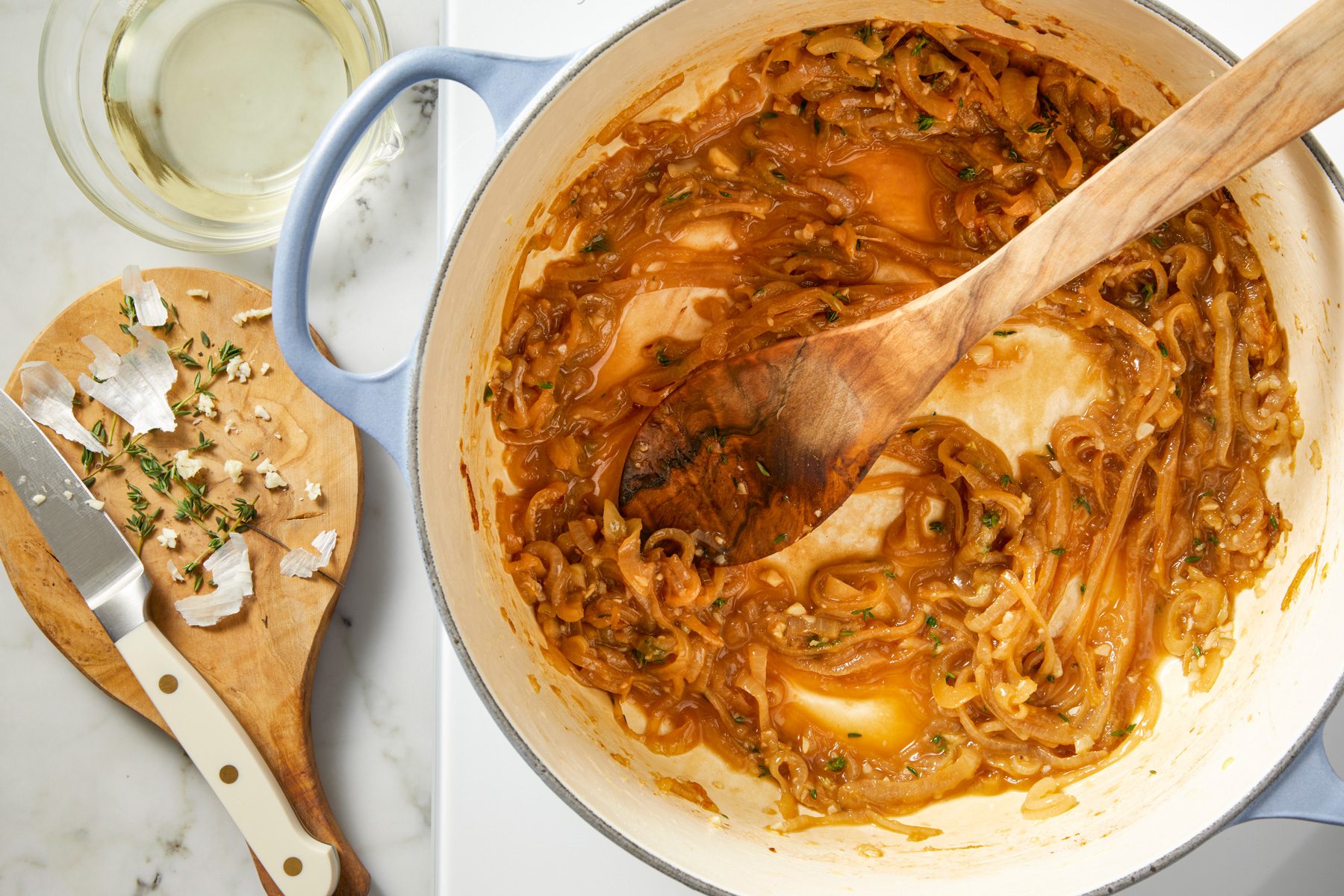 Minced garlic and fresh thyme leaves being added to the caramelized onions in the pot, followed by white wine, simmering and stirring to release the browned bits from the pan.