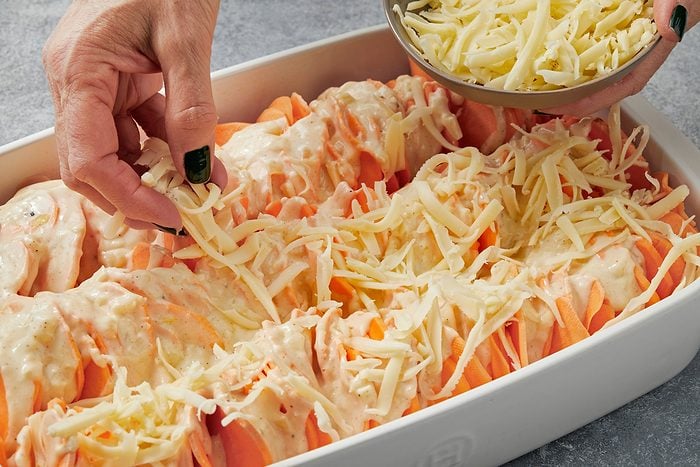 Close up shot of sprinkle remaining 1 cup Gruyere on top; Bake covered 30-35 minutes; Remove covering; bake until cheese is bubbly and golden brown on top 10-15 minutes longer; Let rest 10 minutes before serving; all set on a grey surface