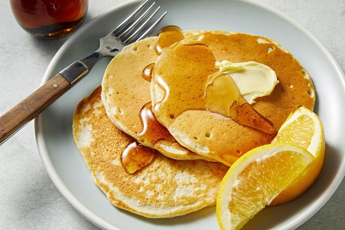 3/4th shot of sourdough pancakes served with a steel fork on a ceramic plate with butter, lemons and honey.