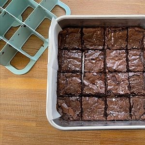 Metal pan of cooked brownies with a grid slicer to the top right