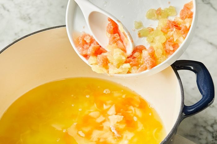 A white bowl with chopped onions and tomatoes is being poured into a large pot containing melted butter or oil on a marble countertop.