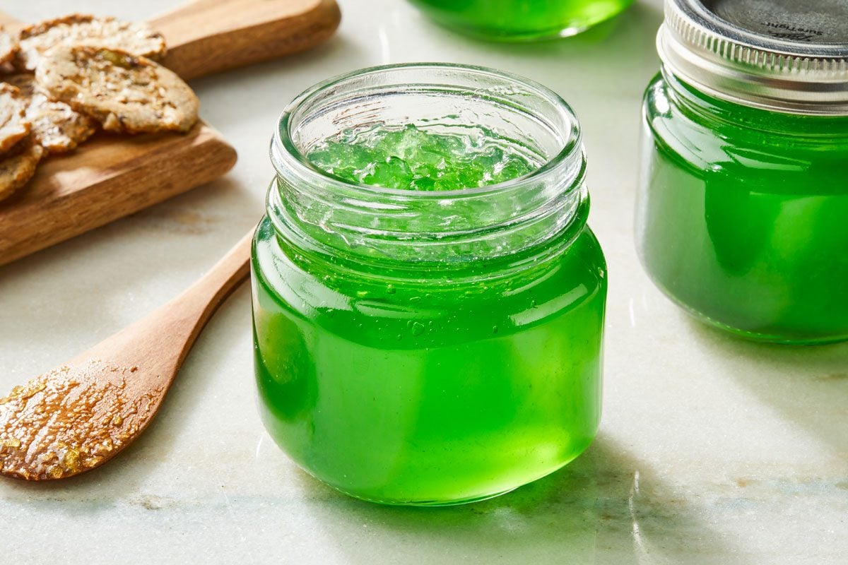 Close shot of Festive Mint Jelly; stored in glass jars; wooden spoon; wooden tray with some crackers; marble surface;