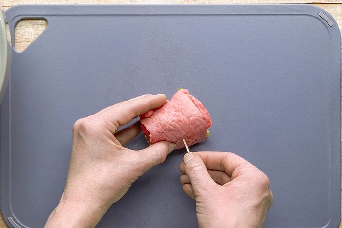Rolling up a piece of meat with filling inside and securing it with a toothpick.