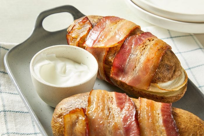 Close-up shot of Bacon-Wrapped Potatoes; served on a tray with choice of dip or sauce on a napkin; empty plates are nearby; all set on a marble surface