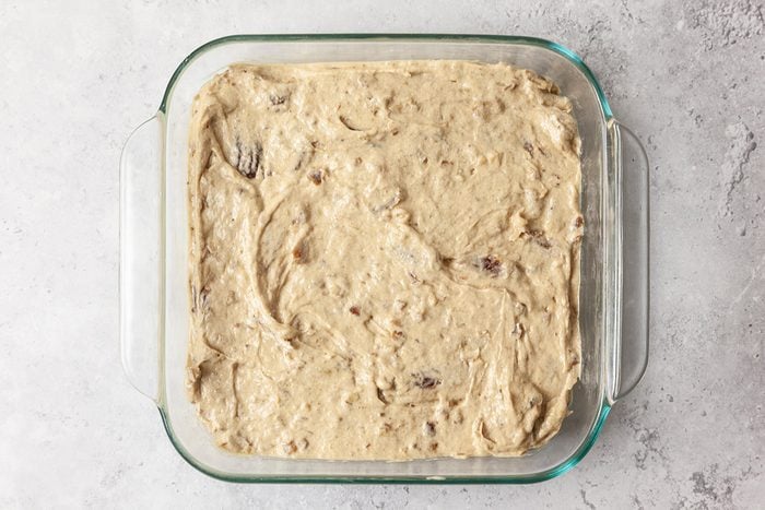 A glass baking dish filled with unbaked cookie dough, spread evenly across the bottom. The dough has a creamy texture with visible chocolate chunks and sits on a light gray countertop.