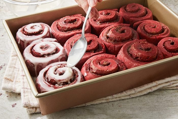 vanilla icing being spooned over baked rolls