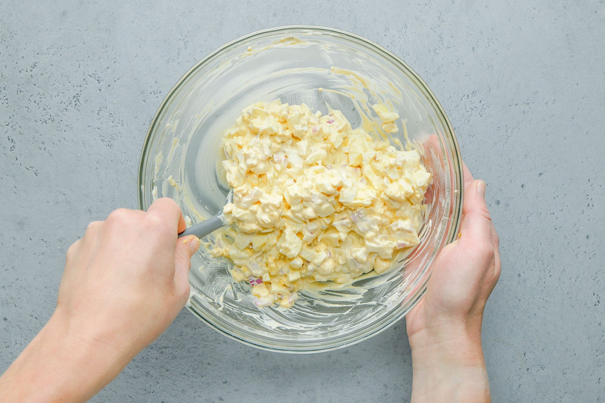 Overhead shot of a small bowl containing the first six ingredients; eggs are added and gently stirred to combine; all set on a grey surface