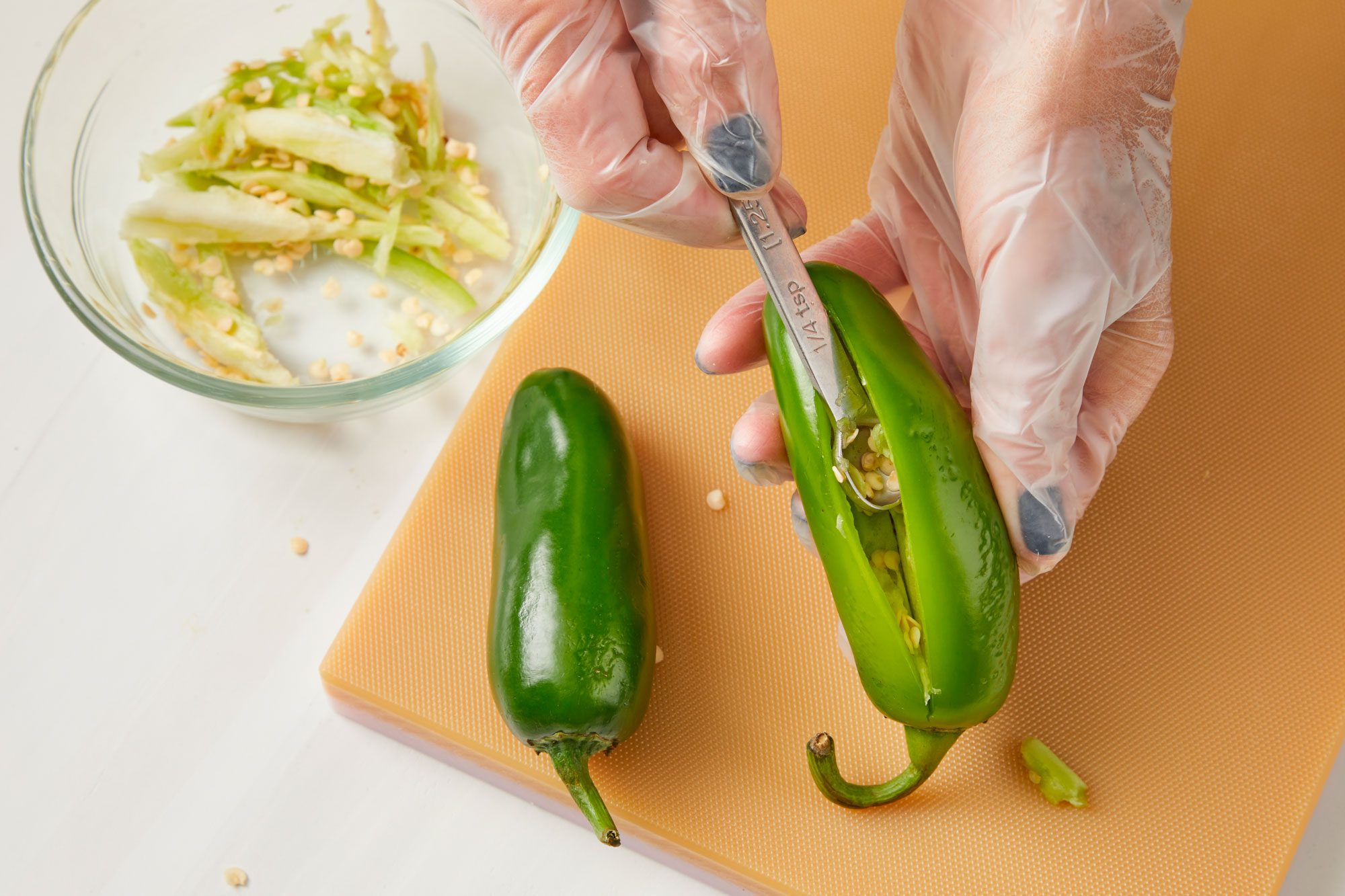 Overhead shot of cut a lengthwise slit down each pepper; leaving the stem intact; remove membranes and seeds; chopping board; all set on a white surface