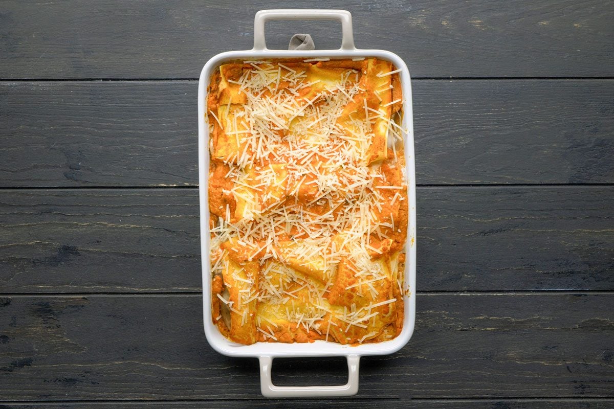 Top Shot of a The white rectangular baking dish contains baked ravioli covered in melted cheese; sitting on a dark wooden surface; presenting a hearty and inviting meal setting