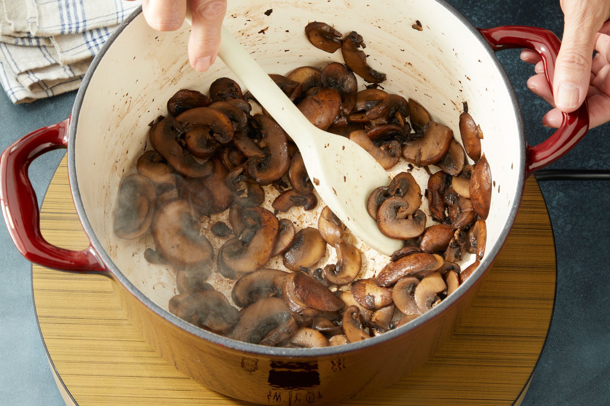 Overhead shot of add mushrooms; cook until tender and edges are brown 5 7 minutes; Remove to a plate; set aside; spoon; induction; napkin; dark surface