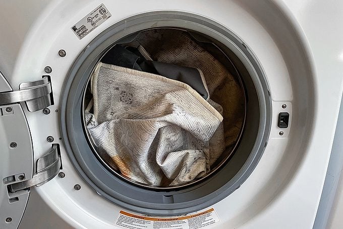Front-loading washing machine with its door open, showing dirty or stained light-colored fabric inside the drum, ready to be washed.