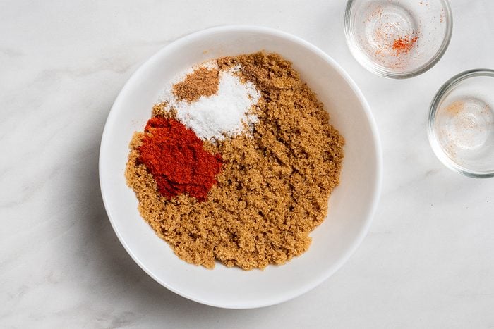 Overhead shot of combining remaining ingredients in a bowl; two empty glass bowls are visible nearby; all set on a white marble surface;