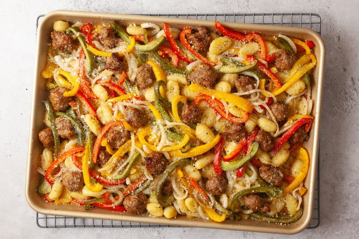 Overhead shot of fully roasted sausage, peppers, onions, and potatoes on a baking sheet with golden, caramelized edges resting on a wired rack