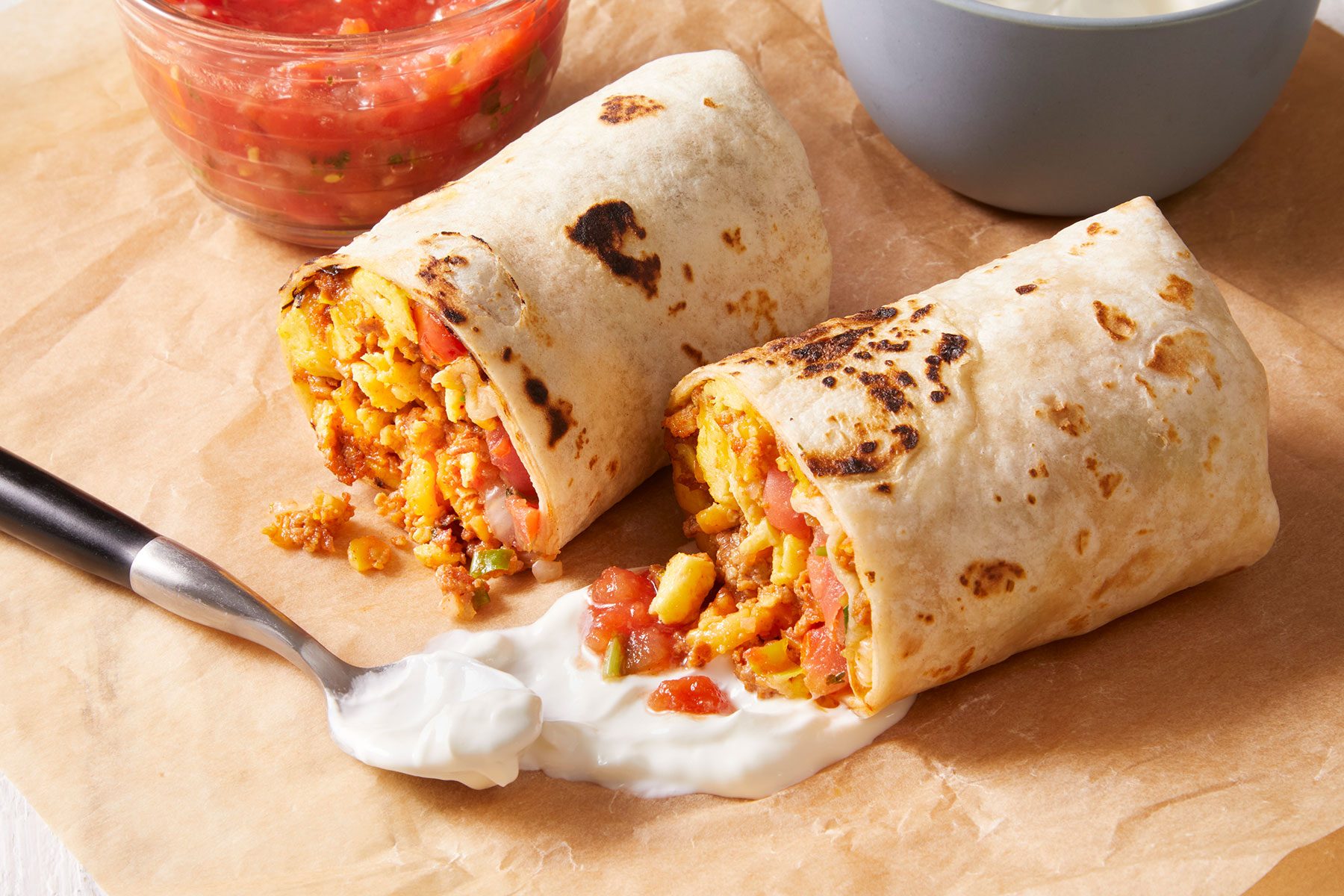 Chorizo Egg Wraps cut into halves with a dip spread with a spoon.