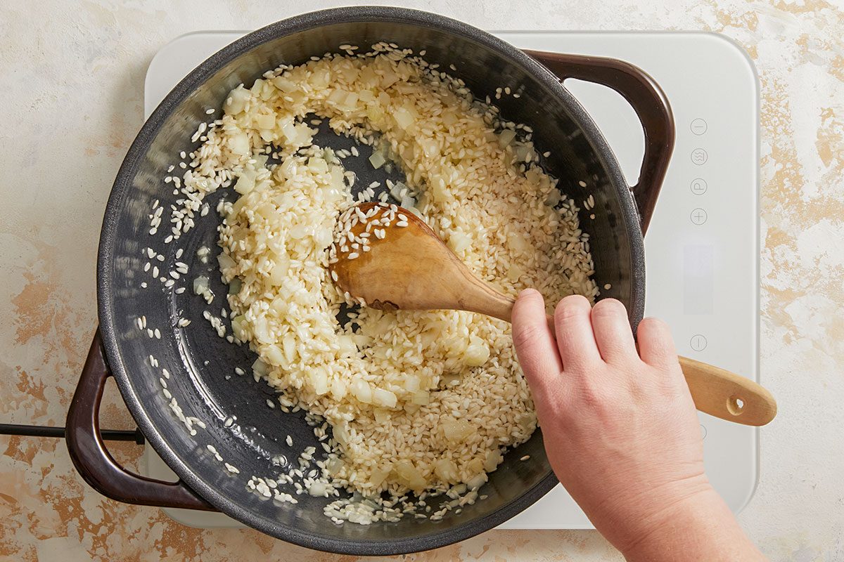 Overhead shot of rice added to the sautéed onions, being stirred together for the risotto base.