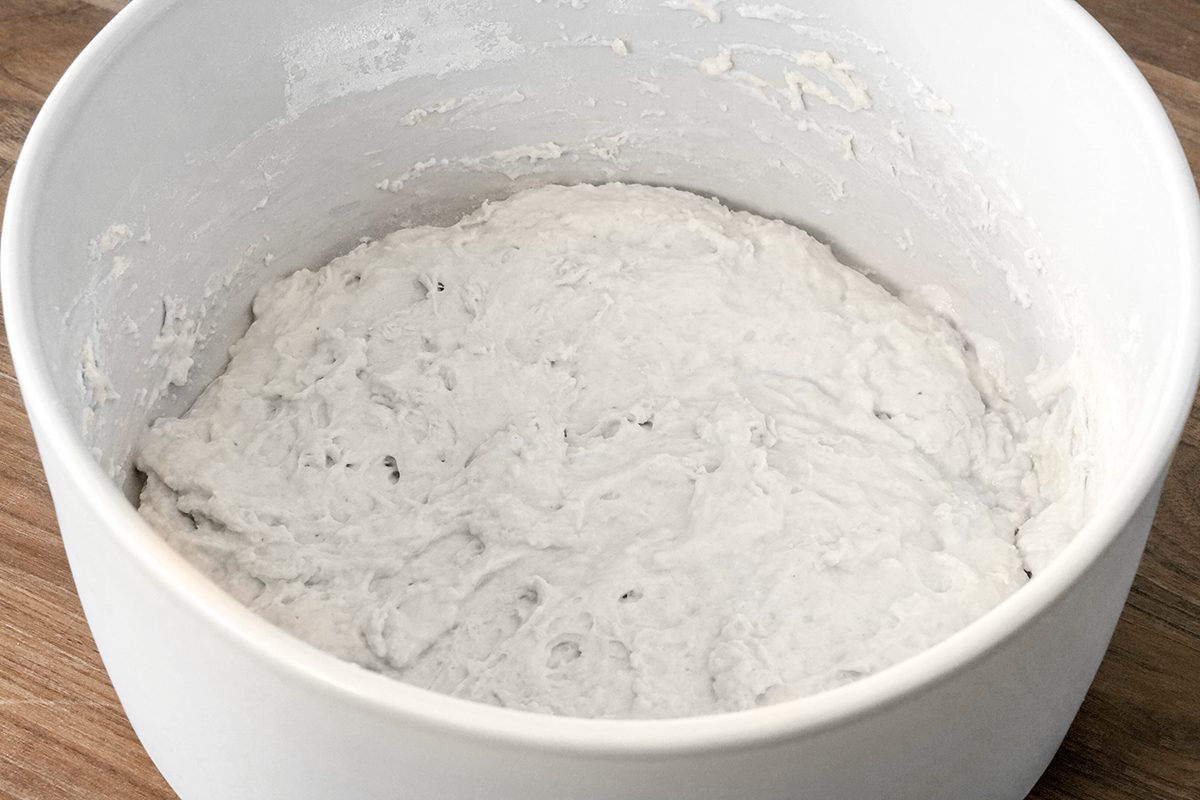 A white ceramic bowl filled with a thick, sticky white dough sits on a wooden surface.