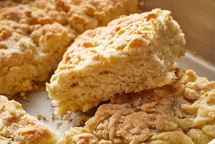 Close-up shot of a close view shows golden brown Butter Swim Biscuits one cut open and raised from the metal tray with a soft flaky layered inside visible