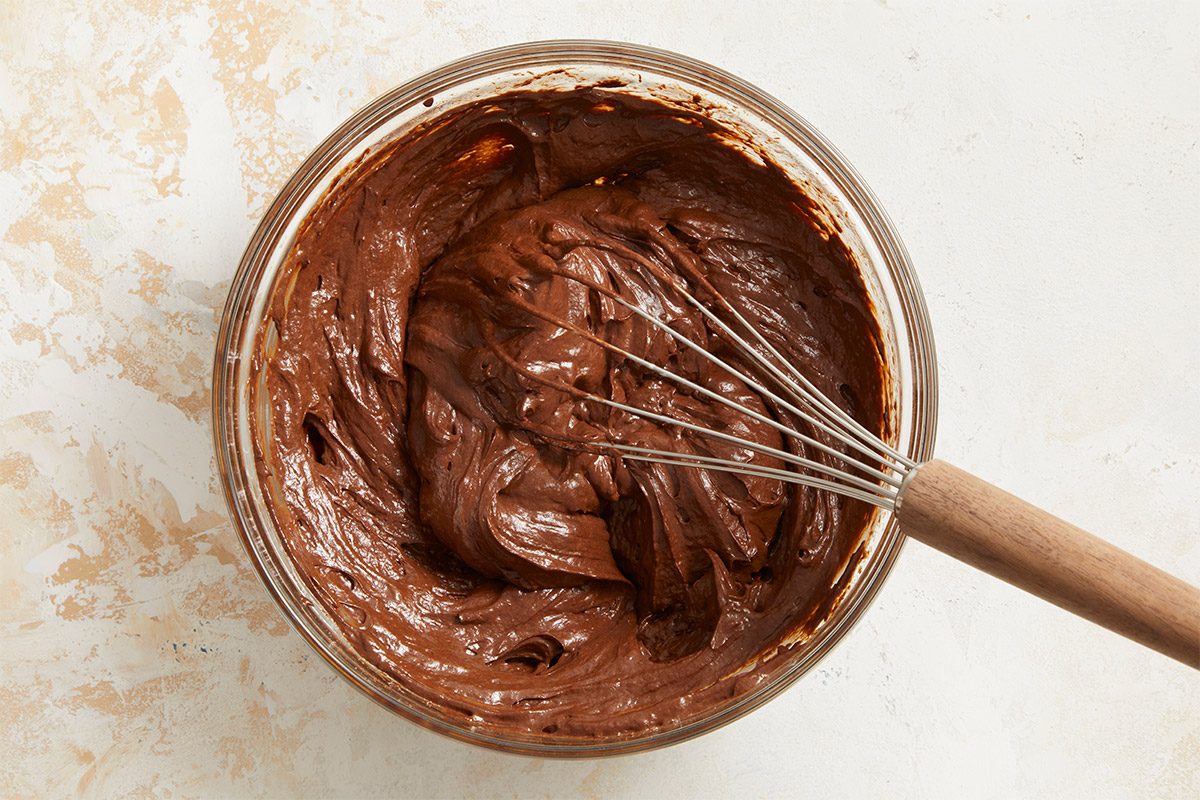 Overhead shot of chocolate brownie batter being whisked in a clear glass bowl;