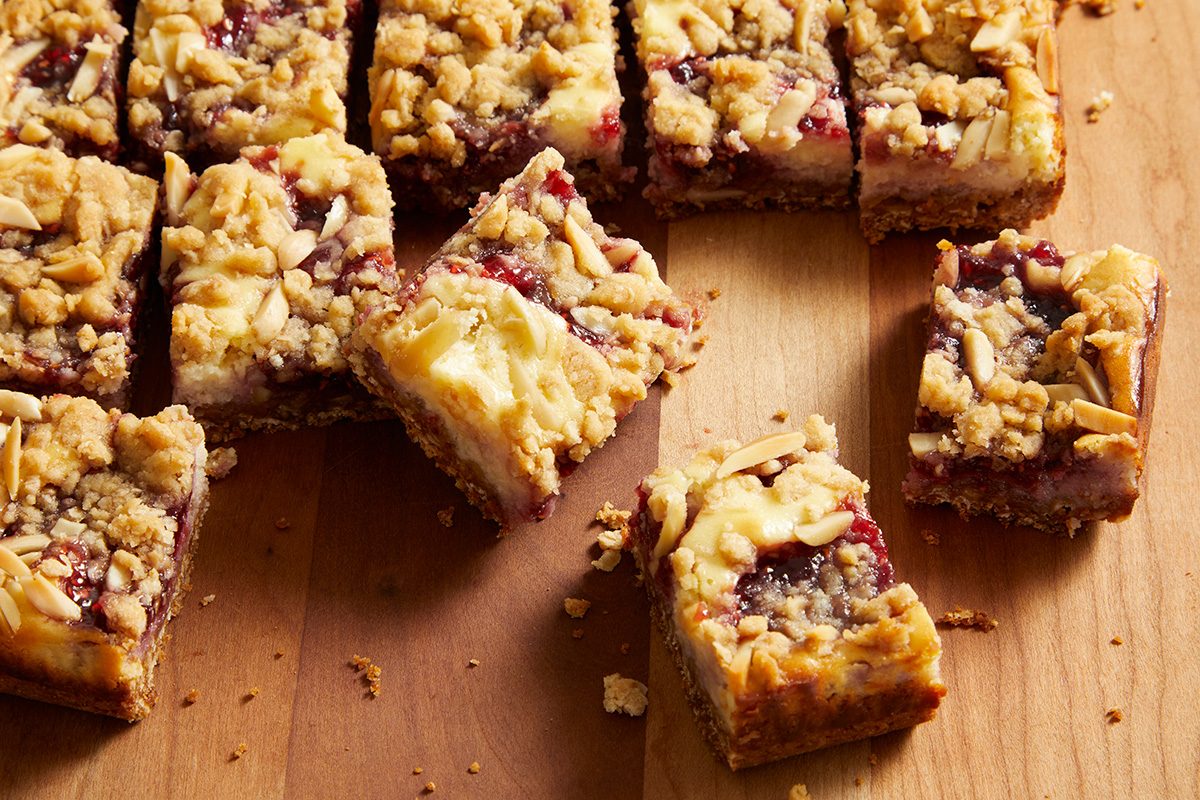 Several dessert bars with a crumbly topping and a visible fruit filling are cut into squares and arranged on a wooden surface. Some bars are slightly separated from the group.
