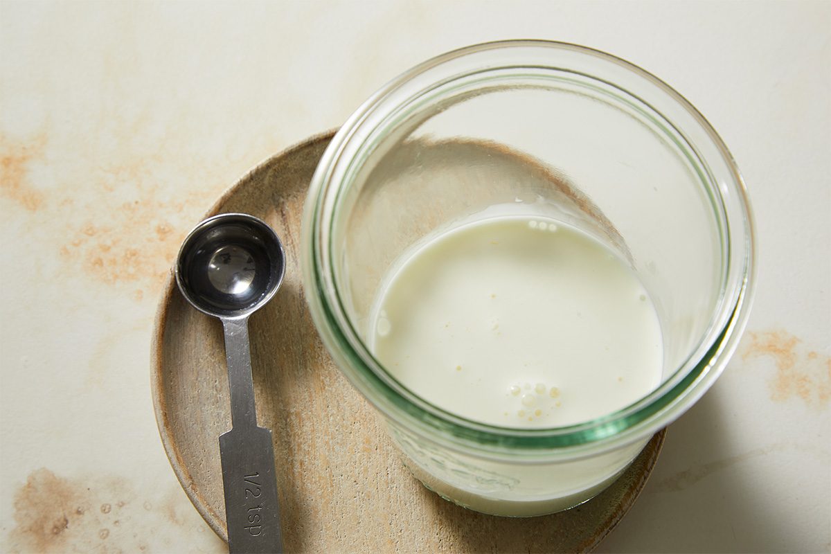 Overhead view of heavy whipping cream measured in a glass jar alongside a measuring spoon, representing the base for the creamy topping used in a Red Velvet Espresso Martini. The setup highlights preparation of the whipped cream component before mixing.