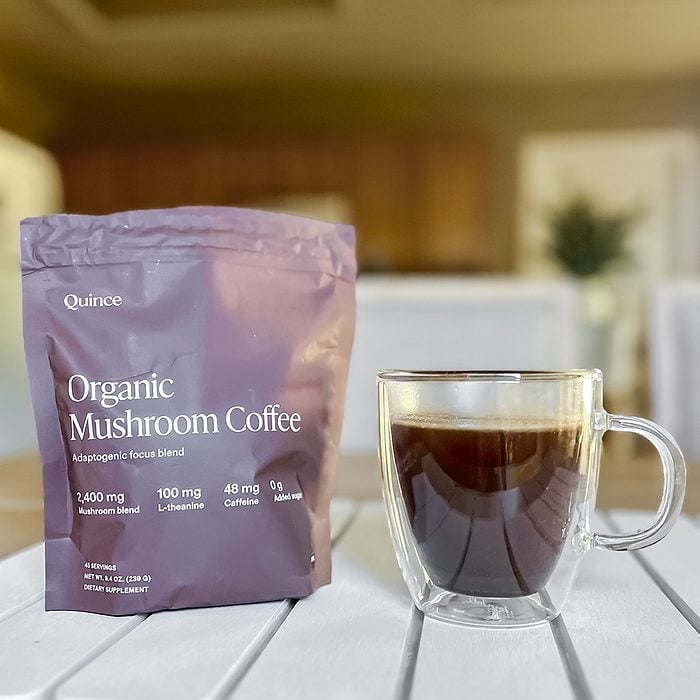 A clear glass mug of black coffee sits on a white table next to a purple bag labeled 