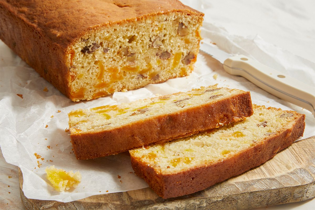 Horizontal composition of apricot bread sliced into thick pieces on parchment paper. The interior crumb reveals visible apricot chunks and chopped nuts.