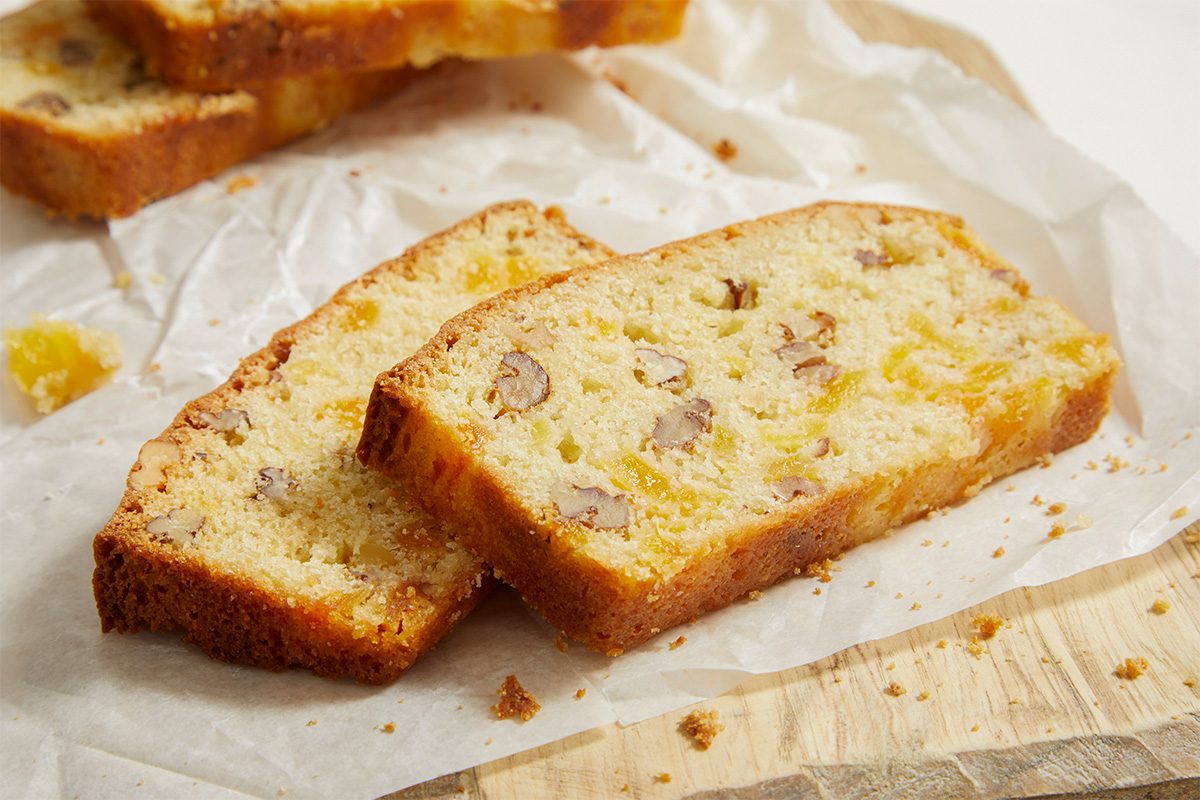 Close-up horizontal image of apricot bread slices stacked on parchment paper. The moist crumb and distribution of dried apricots and nuts are clearly visible.