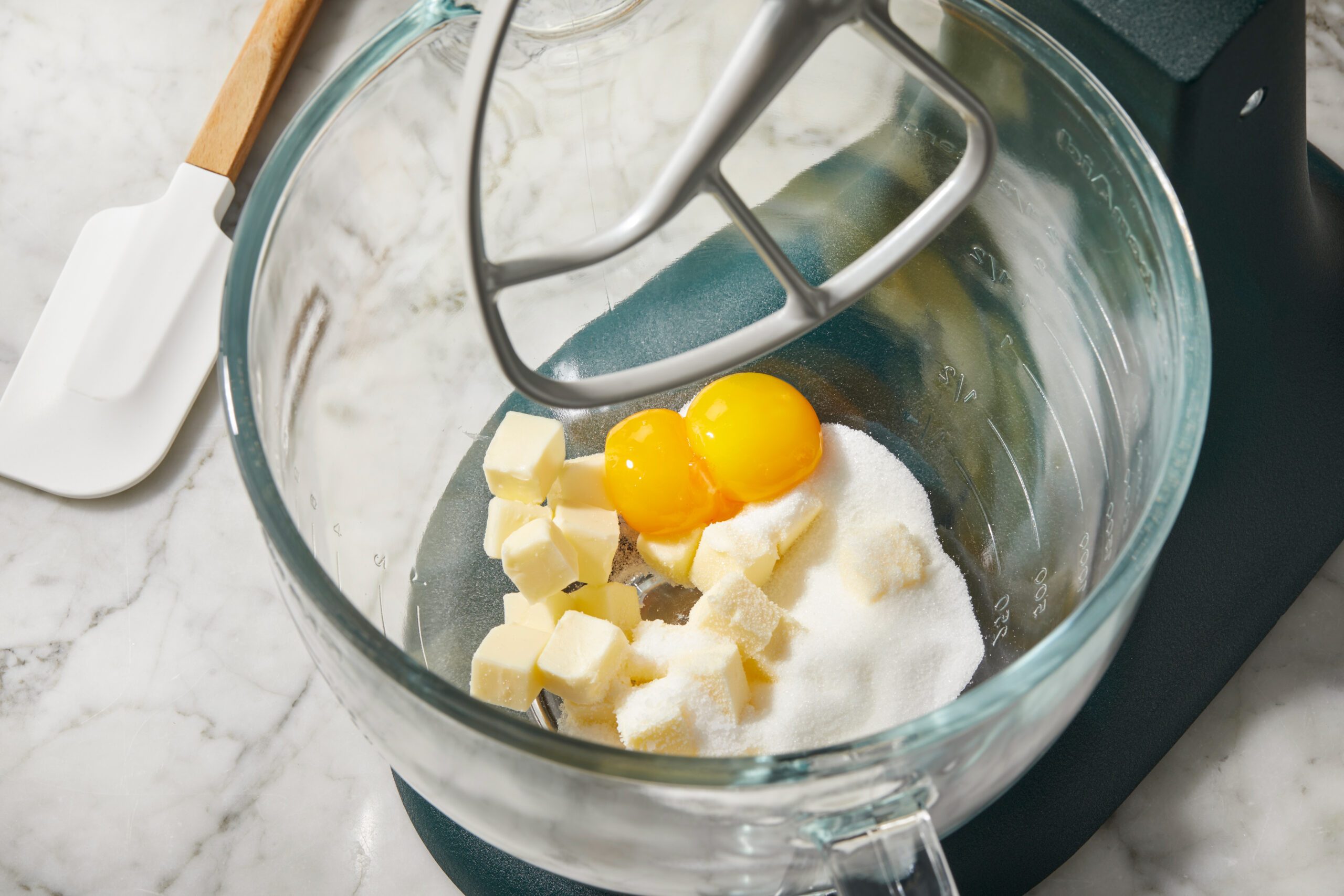 Overhead view of softened butter and egg yolks added to a glass mixing bowl fitted with a mixer attachment, marking the first step in preparing biscuit dough for biscuits de fromage.