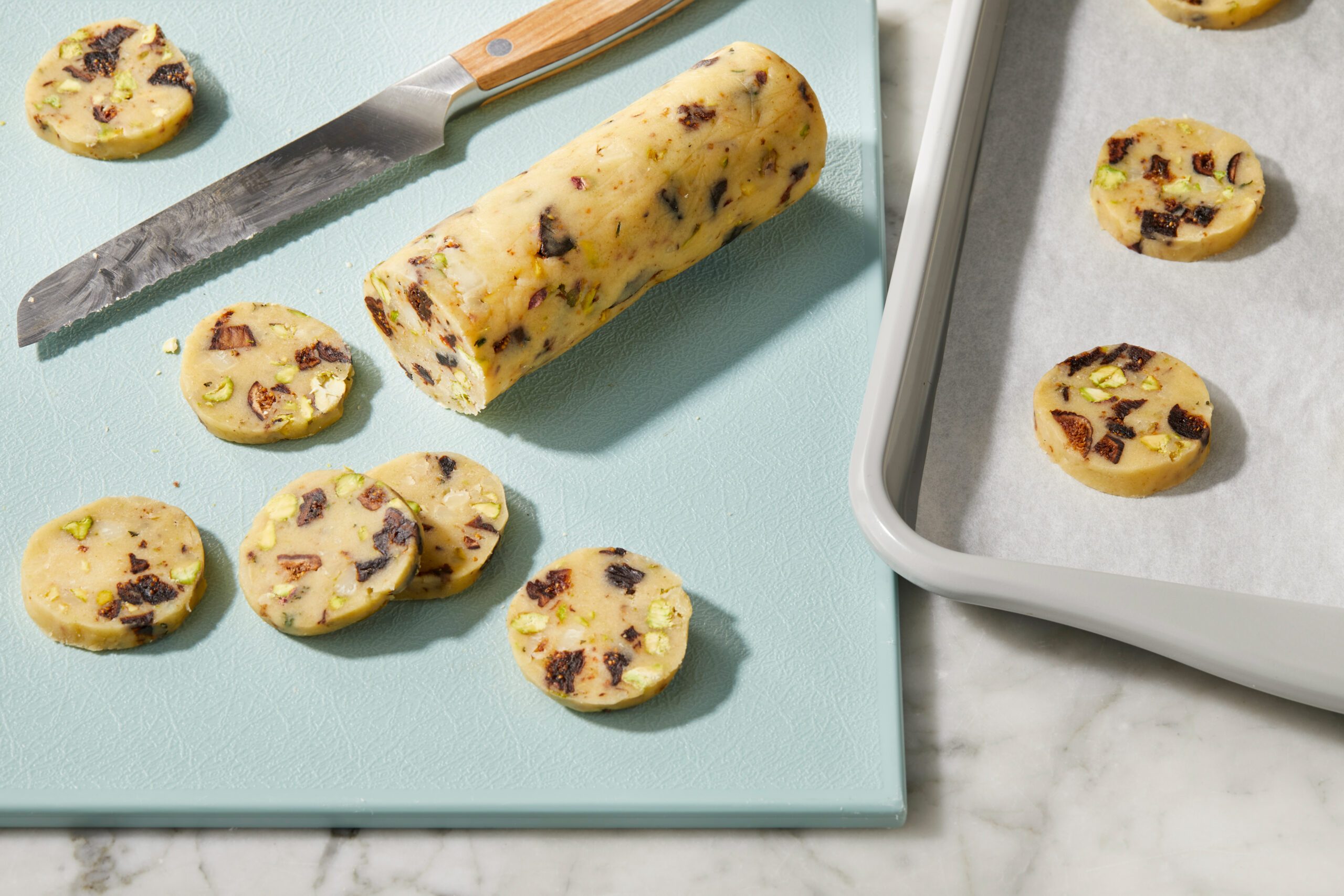 Top-down image of chilled biscuit dough sliced into rounds on a cutting board, with a knife and baking tray nearby for the next baking step.