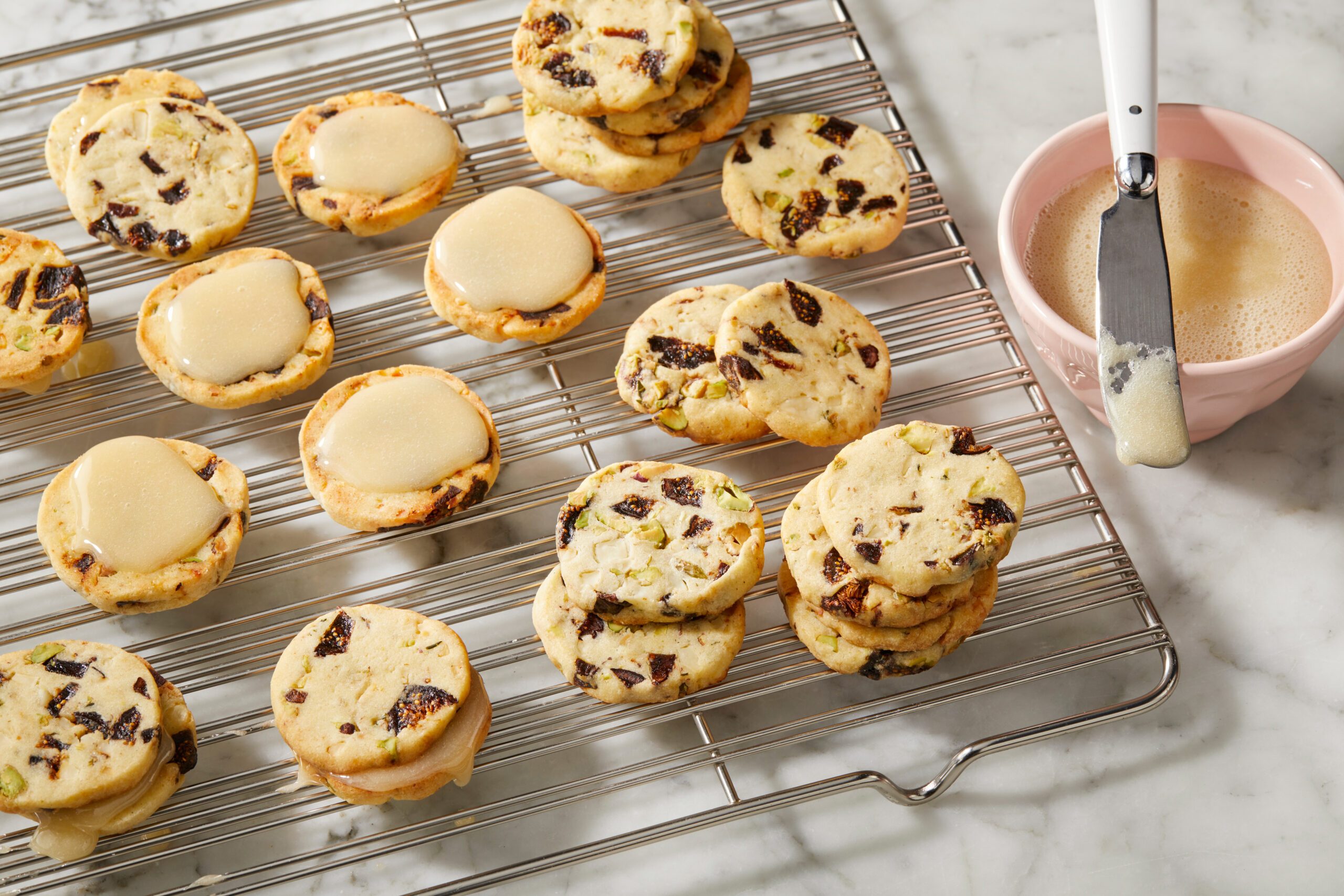 Overhead view of baked biscuits cooling on a wire rack, with honey being spooned onto the centers in preparation for sandwiching.