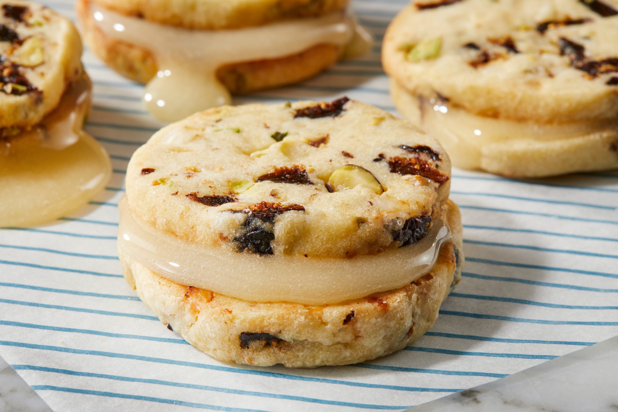 Overhead close-up of a biscuit de fromage sandwich cookie filled with honey, showing layers of cheese biscuit and visible fig and pistachio pieces.