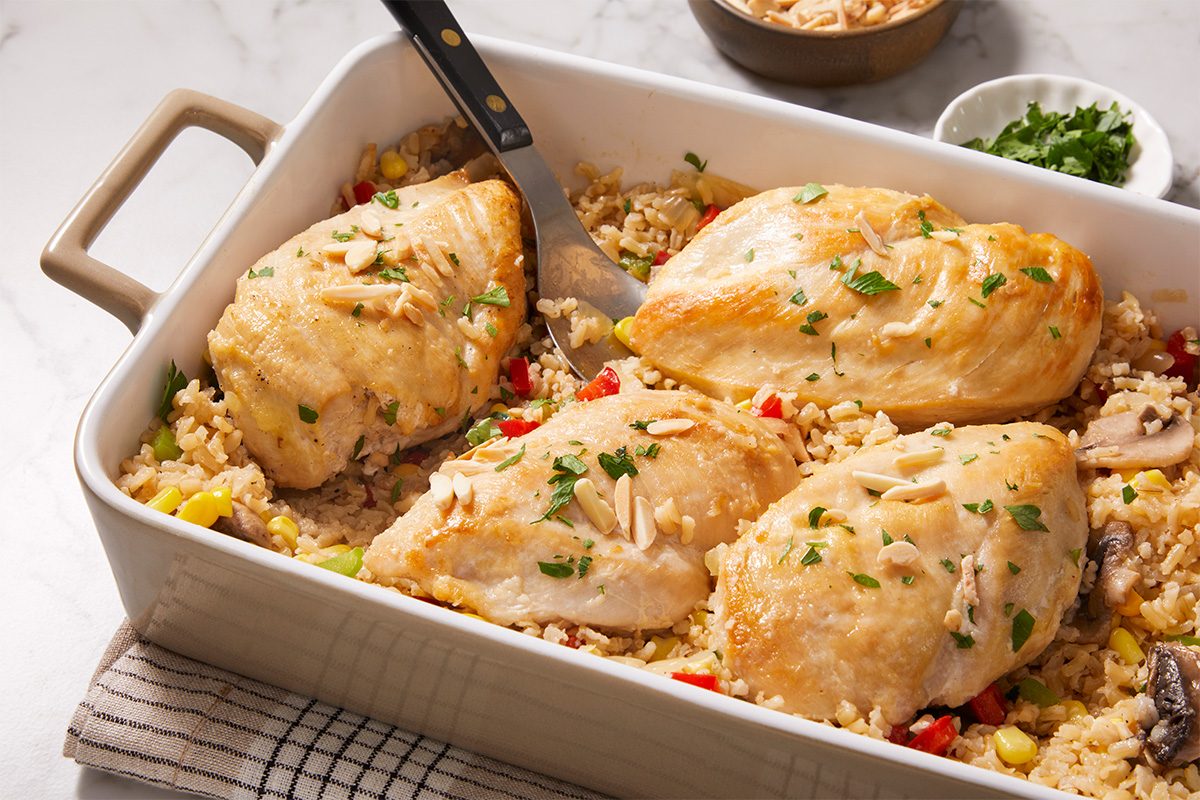Closeup shot of chicken rice casserole with vegetables in a baking dish, garnished with slivered almonds and parsley;