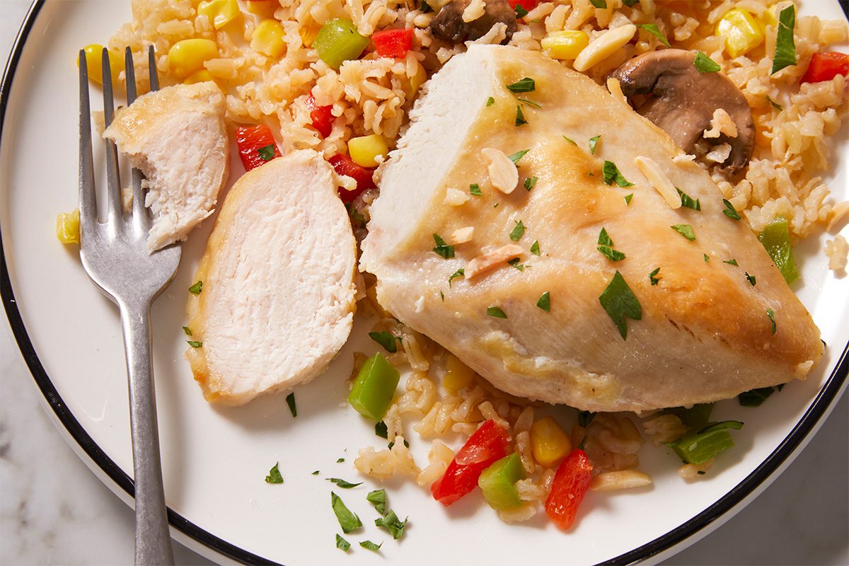 Closeup shot of plated chicken rice casserole with vegetables, garnished with parsley and slivered almonds, with a fork resting on the plate;