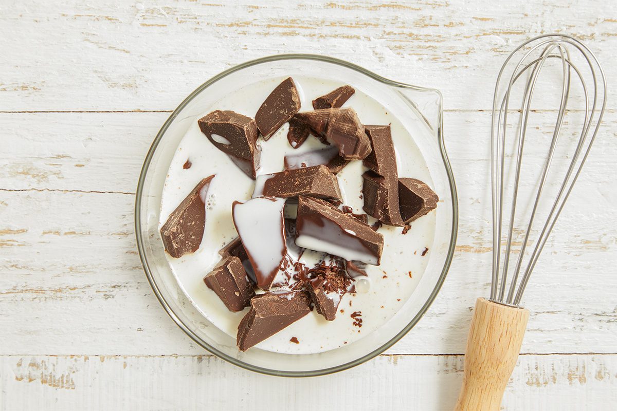 Overhead view of chopped semisweet chocolate on a plate with whisk nearby, preparing ganache garnish for the finished cake.