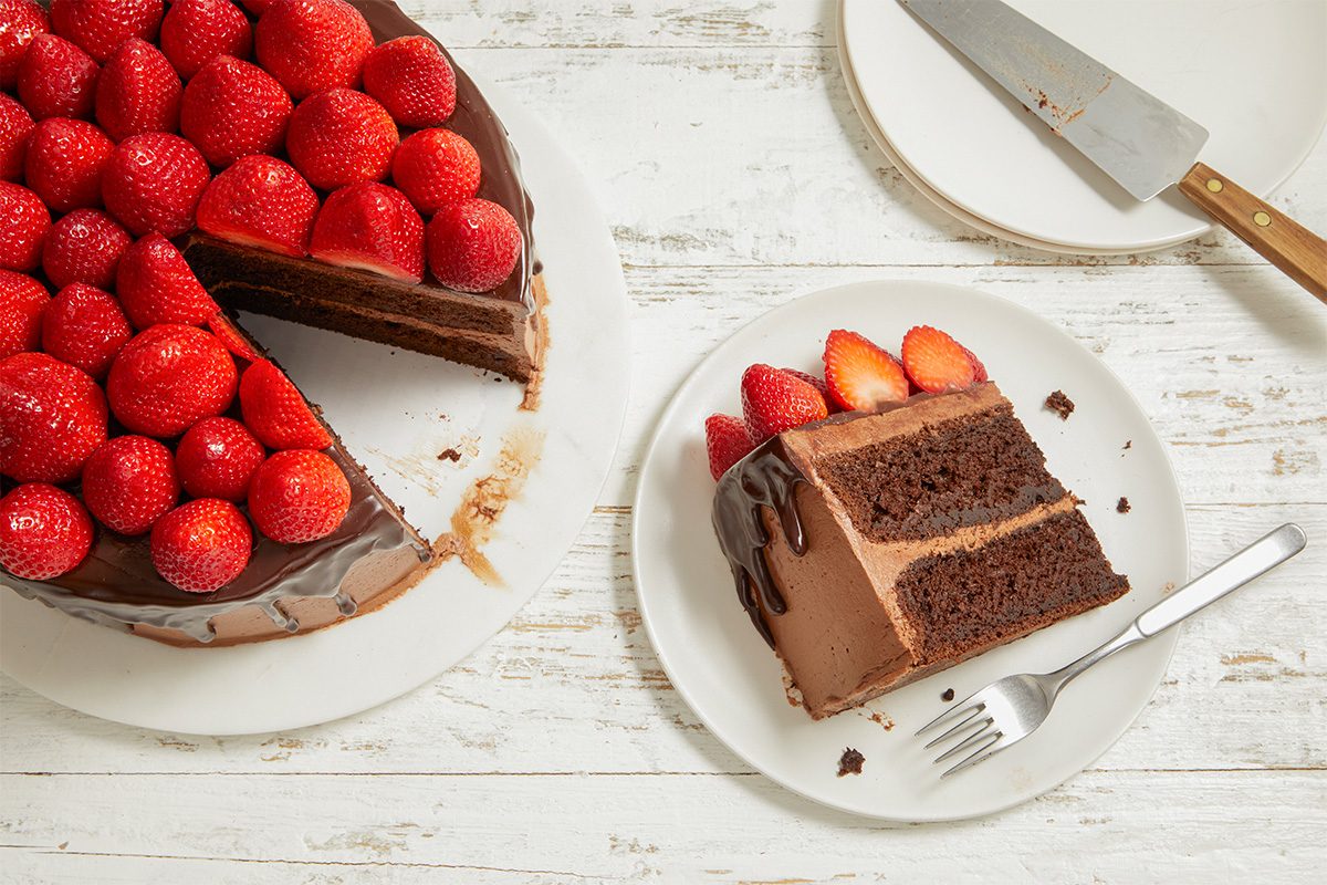 Overhead image of the chocolate-strawberry cake with one slice removed, revealing the layered interior. A plated slice sits beside the remaining cake.