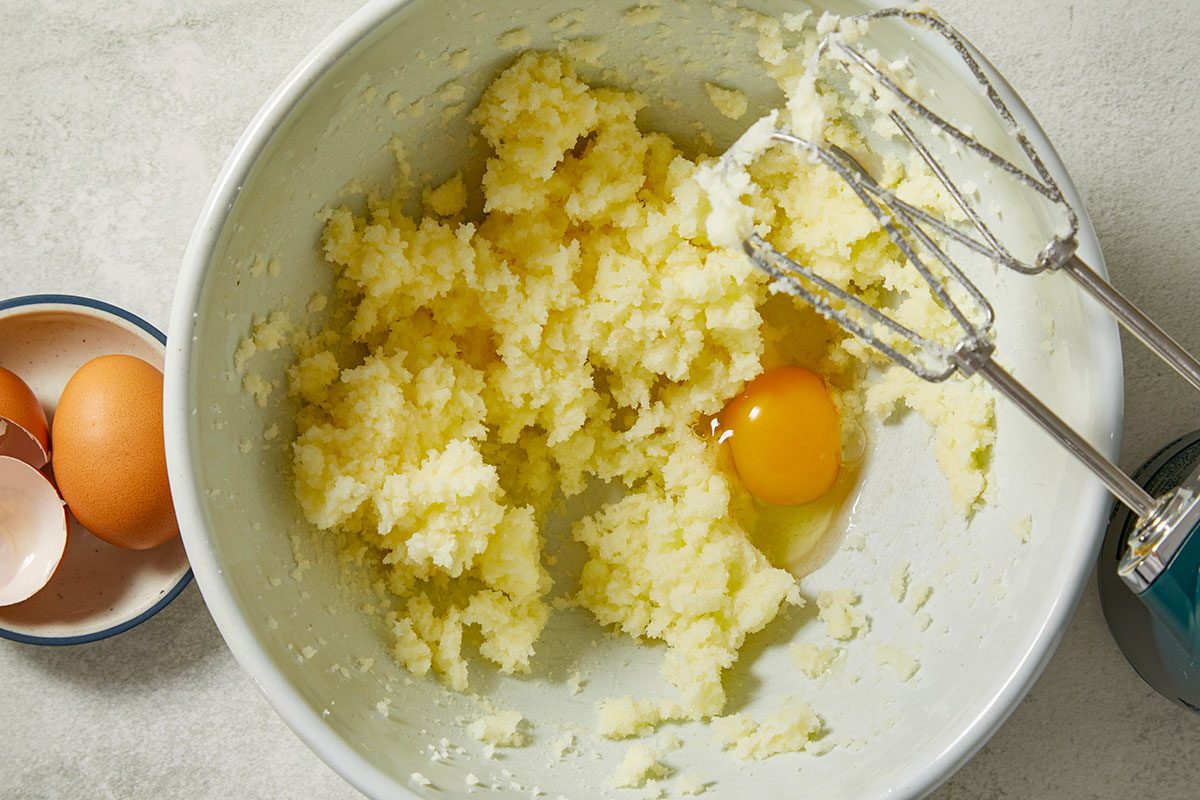 Overhead view of softened butter and sugar being creamed together with eggs in a mixing bowl for Creme Brulee Cupcakes. Fresh vanilla beans are visible alongside the mixer, highlighting the rich vanilla flavor base of the cupcake batter.