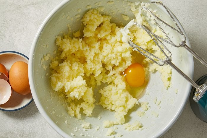 Overhead view of softened butter and sugar being creamed together with eggs in a mixing bowl for Creme Brulee Cupcakes. Fresh vanilla beans are visible alongside the mixer, highlighting the rich vanilla flavor base of the cupcake batter.
