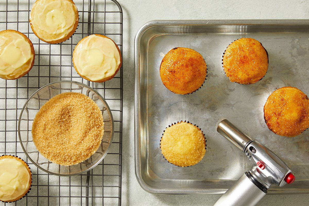 Overhead view of baked cupcakes on a wire rack with centers removed to prepare for filling with pastry cream.