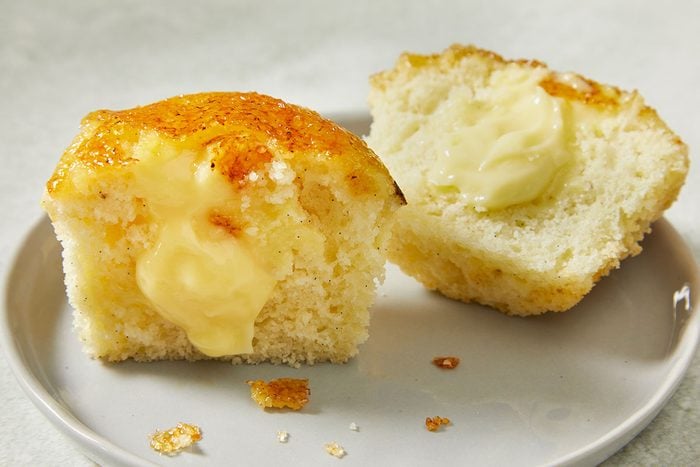 Overhead close-up of a Creme Brulee Cupcake split open to reveal smooth pastry cream filling beneath the crisp caramelized sugar topping.