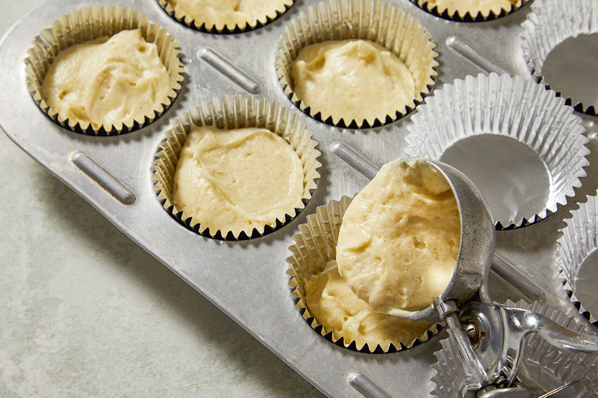Overhead shot of cupcake liners in a muffin tin being filled with smooth vanilla batter, ready to bake into tender cupcakes.