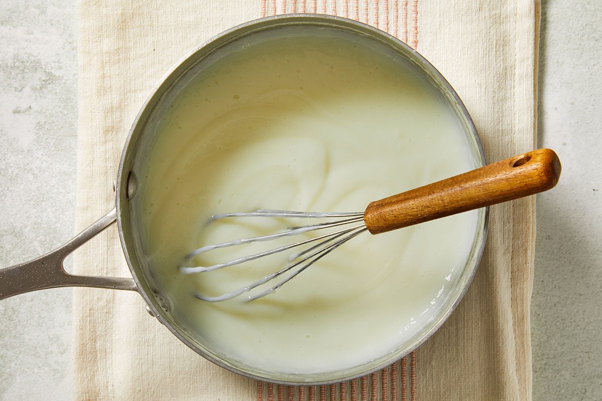 Overhead image of whole milk gently heating in a saucepan with a whisk, beginning the pastry cream for the cupcake filling.