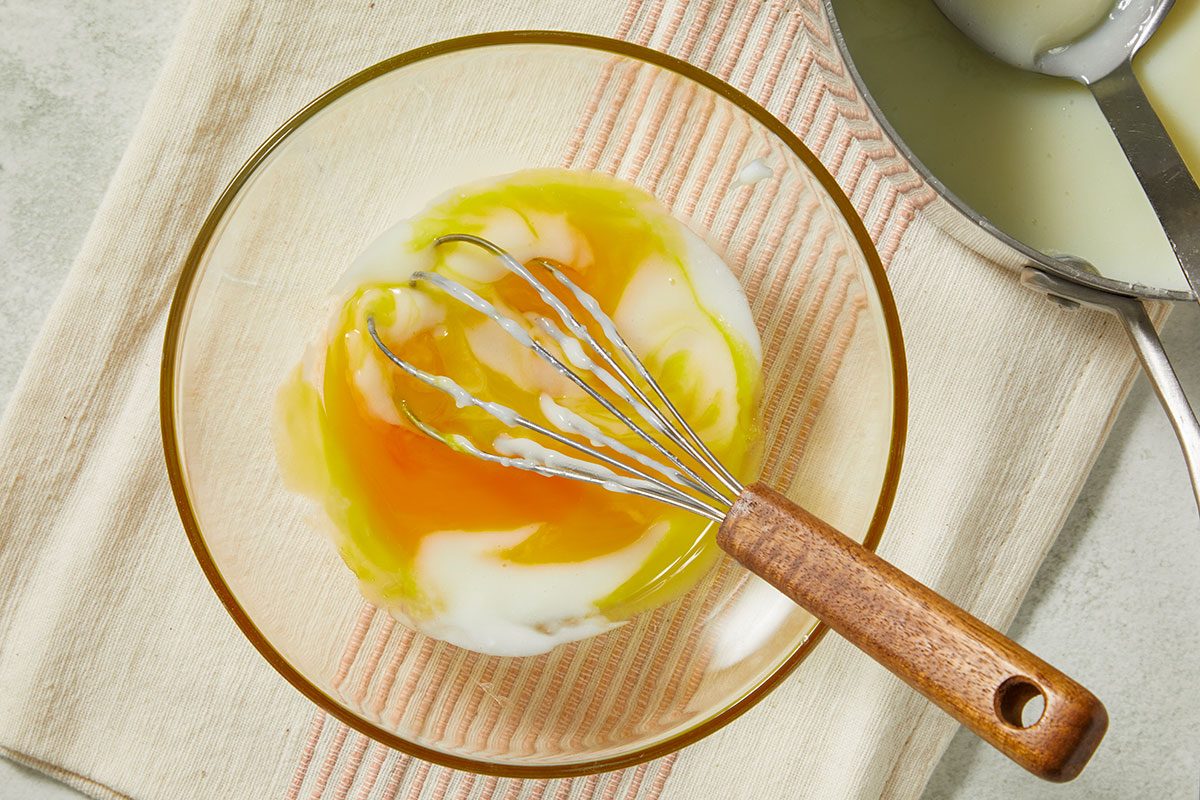 Overhead view of egg yolks whisked with sugar and cornstarch to create the base for pastry cream before tempering with hot milk.