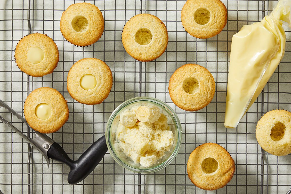 Overhead view of baked cupcakes on a wire rack with centers removed to prepare for filling with pastry cream.