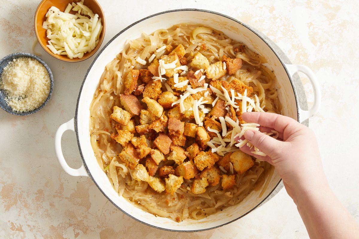 croutons added to onion mixture being sprinkled with cheese