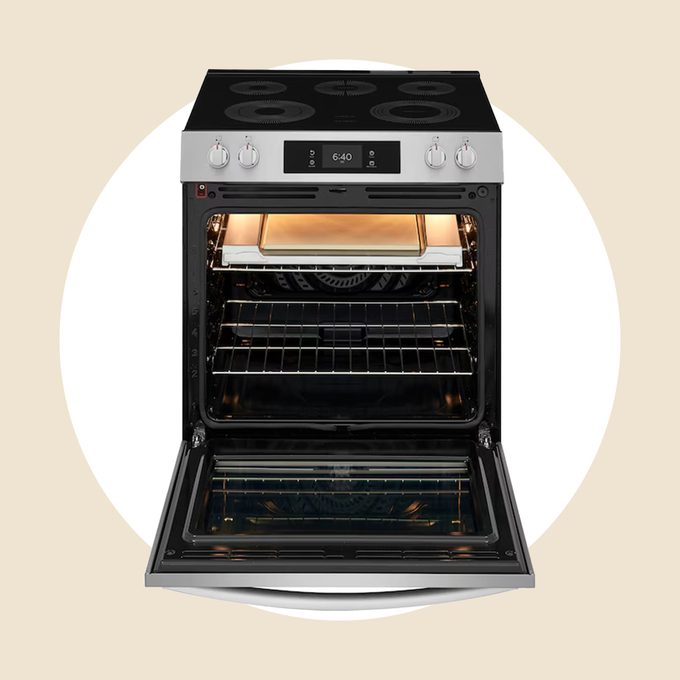 A modern electric oven with a digital display and a glass door is open, revealing multiple racks and a baking tray inside. The oven light is on, illuminating the interior.