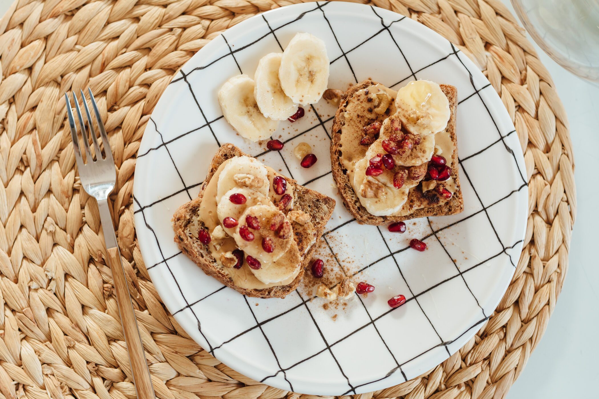 Shot of the peanut butter toast with banana slices and pomegranate on a plate.